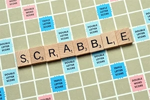 Puiset kirjainlaatat muodostavat sanan SCRABBLE pelilaudalla, jossa on erivärisiä pisteitä