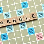 Puiset kirjainlaatat muodostavat sanan SCRABBLE pelilaudalla, jossa on erivärisiä pisteitä